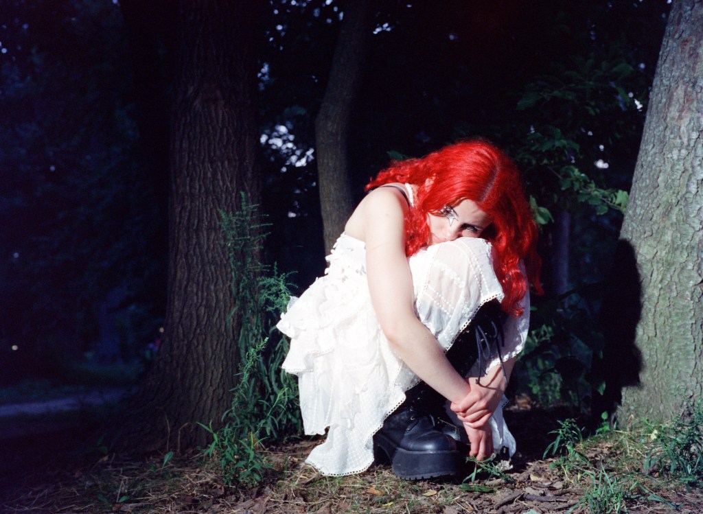Nectarine Girl crouched in front of some trees