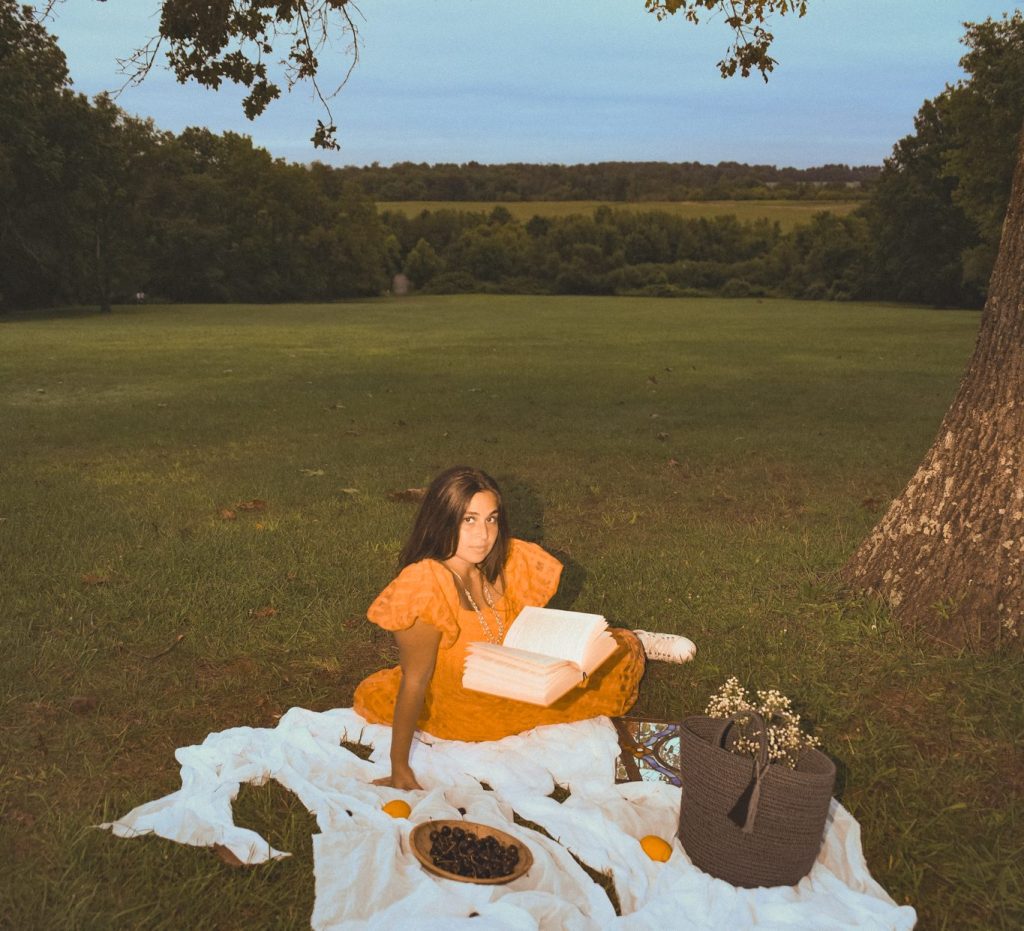 Chiara Maria sitting in a field with a book in her lap.