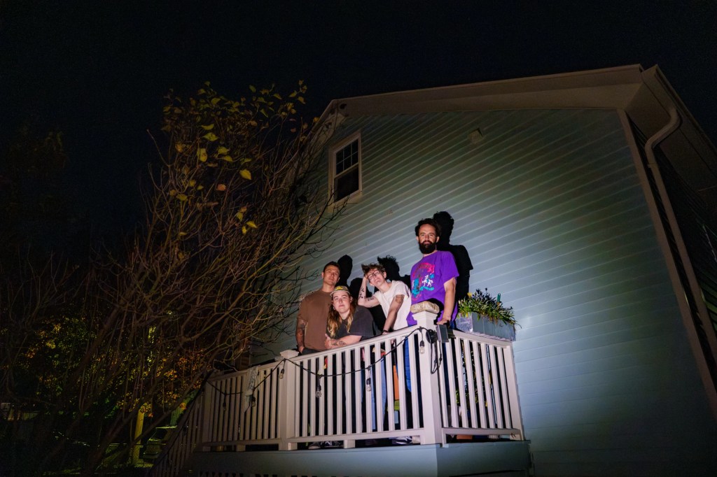 The members of Future Teens stand on a balcony with a spotlight pointed at them