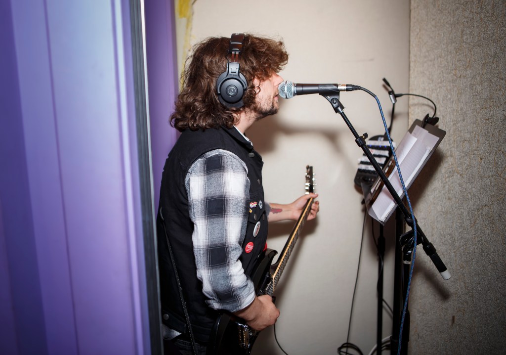 Bobby Mahoney in the recording studio, standing in front of a microphone and holding a guitar