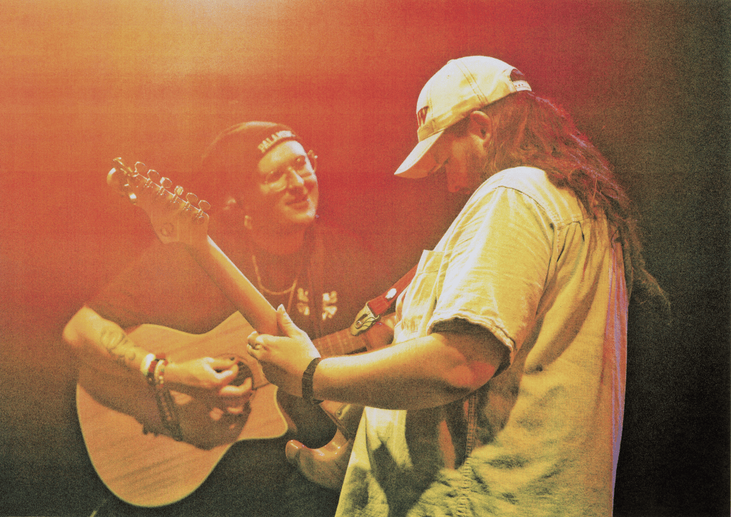 Two men play guitar together